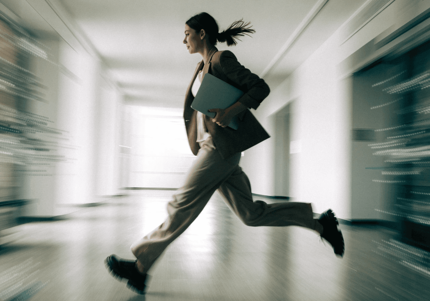 Businesswoman in motion, holding a laptop, running through an office hallway.
